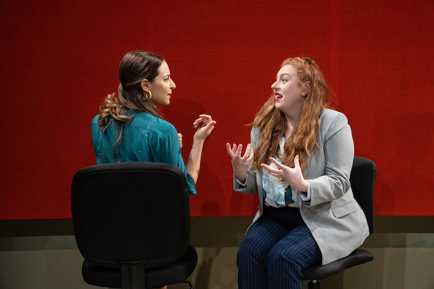 A woman in a swivel chair with her back to the camera speaking with another woman in a swivel chair. 