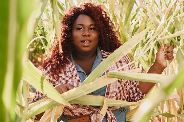 A woman peers through rows of corn. 