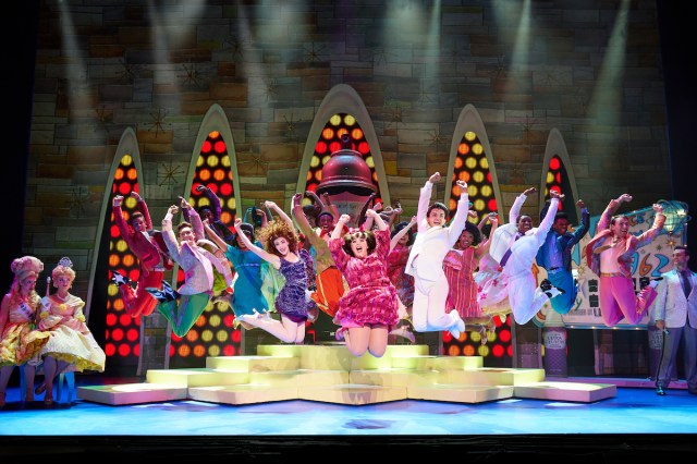 Brightly costumed actors leap in the air simultaneously. 