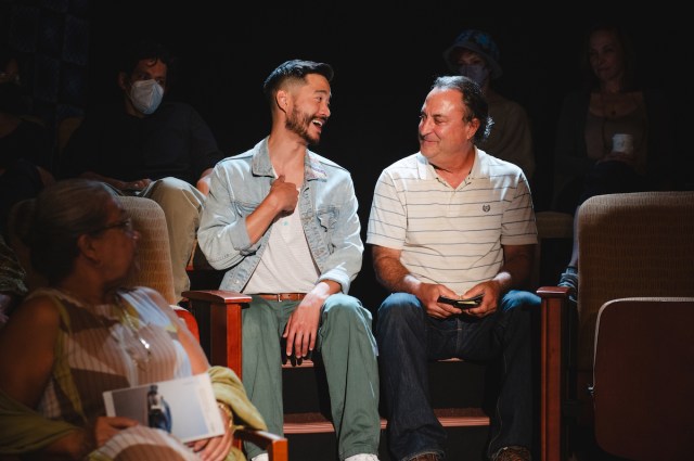 Two men chat in theater seats. 