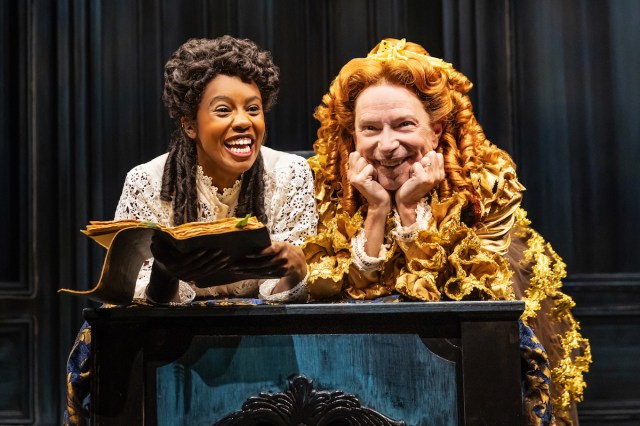 A woman and a man in drag look positively delighted as they hover over a book. 