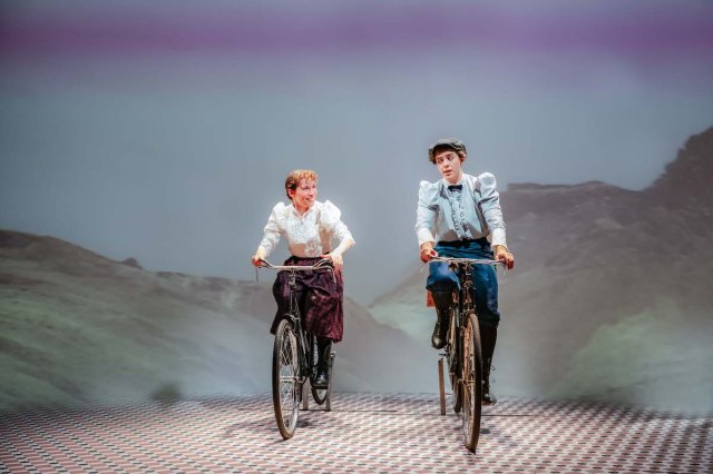 Two women ride bicycles toward the camera. 